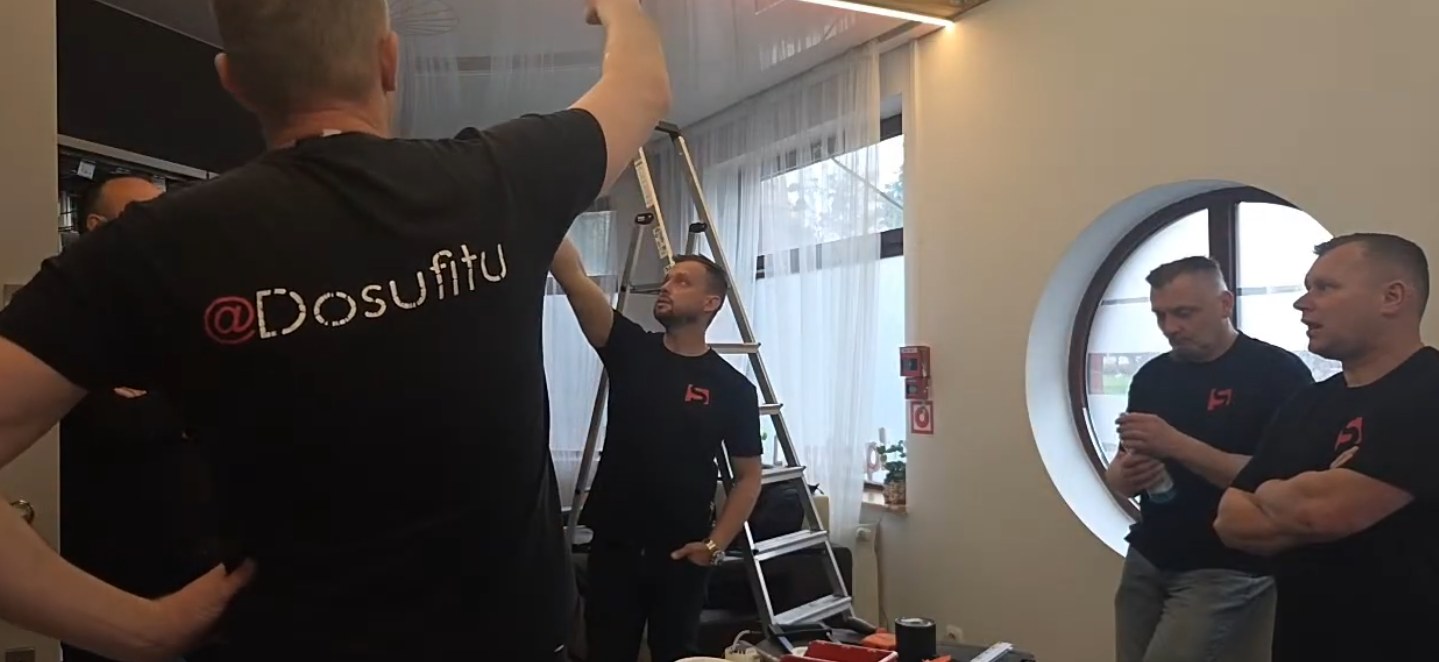 Instruktor pokazuje uczestnikom sufit napinany w sali szkoleniowej